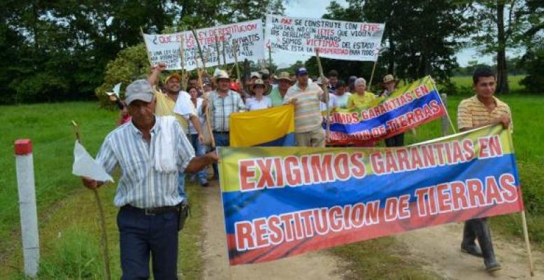 campesinos manifestando por sus tierras. una bandera de colombia dice: exigimos garantias en restitucion de tierras