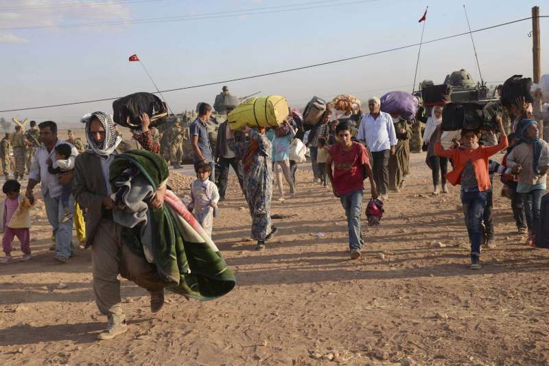 sirios a pie huyen por un terreno desertico. llevan sus pertenencias a cuestas. se ven de todas las edades
