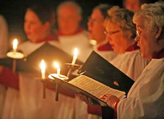 varias personas cantan en un coro durante una celebracion. sostienen velas encendidas.
